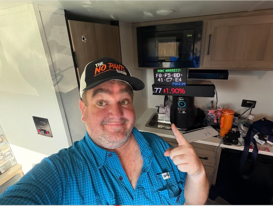 Richard in RV kitchen pointing at crypto ticker displays